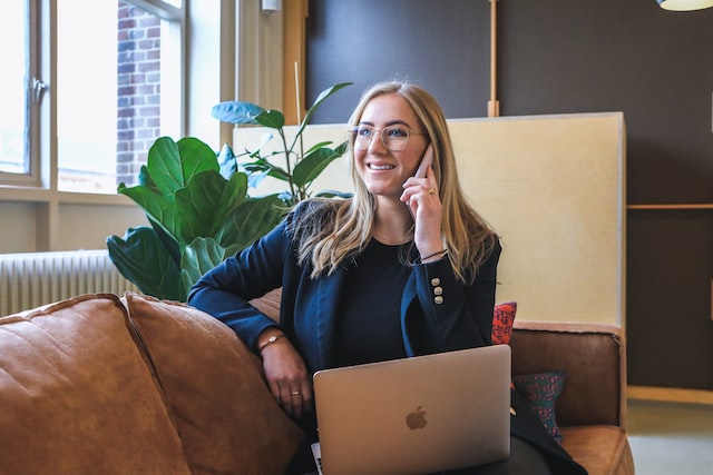 Property manager with blonde hair sitting on a leather couch talking on the phone